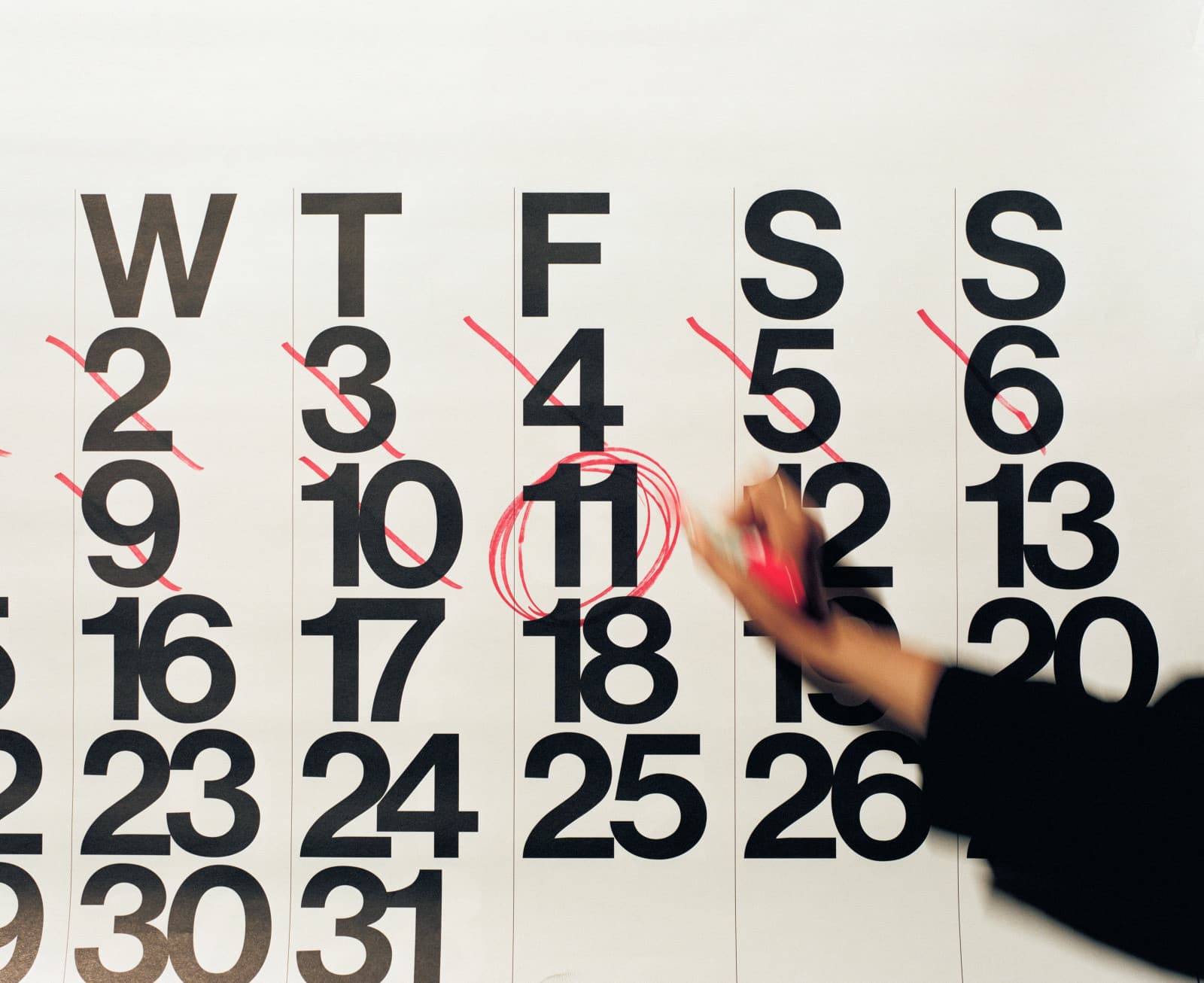 Mão com marcador vermelho circulando o dia 11 em um grande calendário de parede, dias anteriores riscados